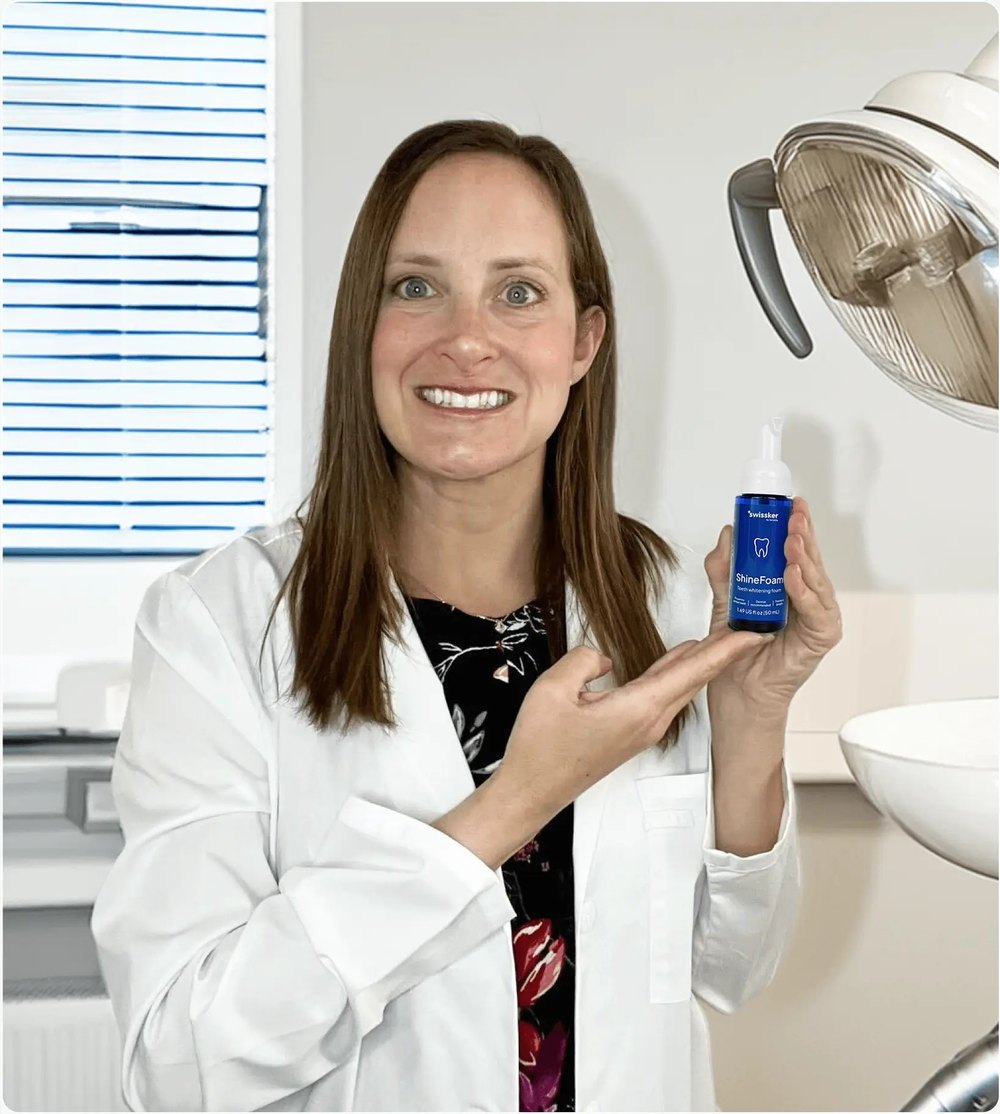 Dentist in a white coat holding a bottle of Swissklip ShineFoam in a dental office