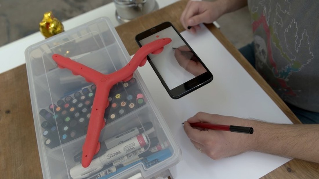 A Tenikle mount holding a phone above a desk to film someone drawing