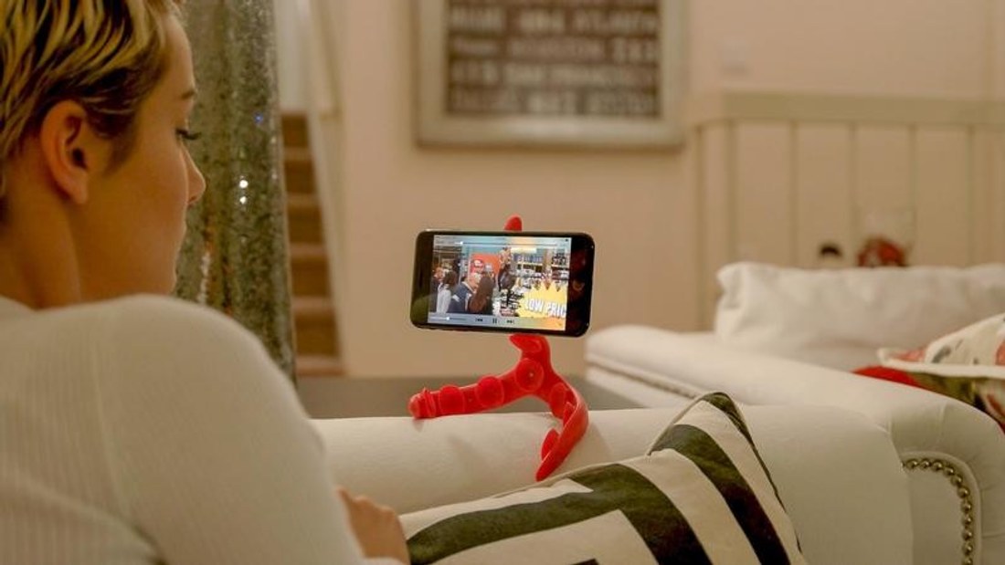 A person on a couch watching video on a phone held by a Tenikle flexible suction mount