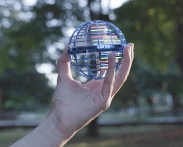 Hand holding the Orbi Boomerang Ball with its colored LED lights glowing through the caged shell