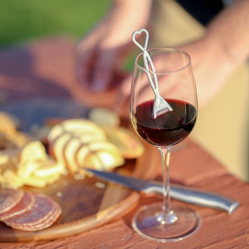 The Wand wine purifier resting in a glass of red wine beside a charcuterie board