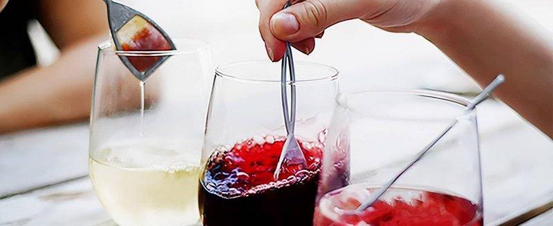 A hand stirring The Wand wine purifier through glasses of white, red, and rose wine