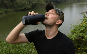 A person drinking from the black UVBrite Smart Bottle beside a lake