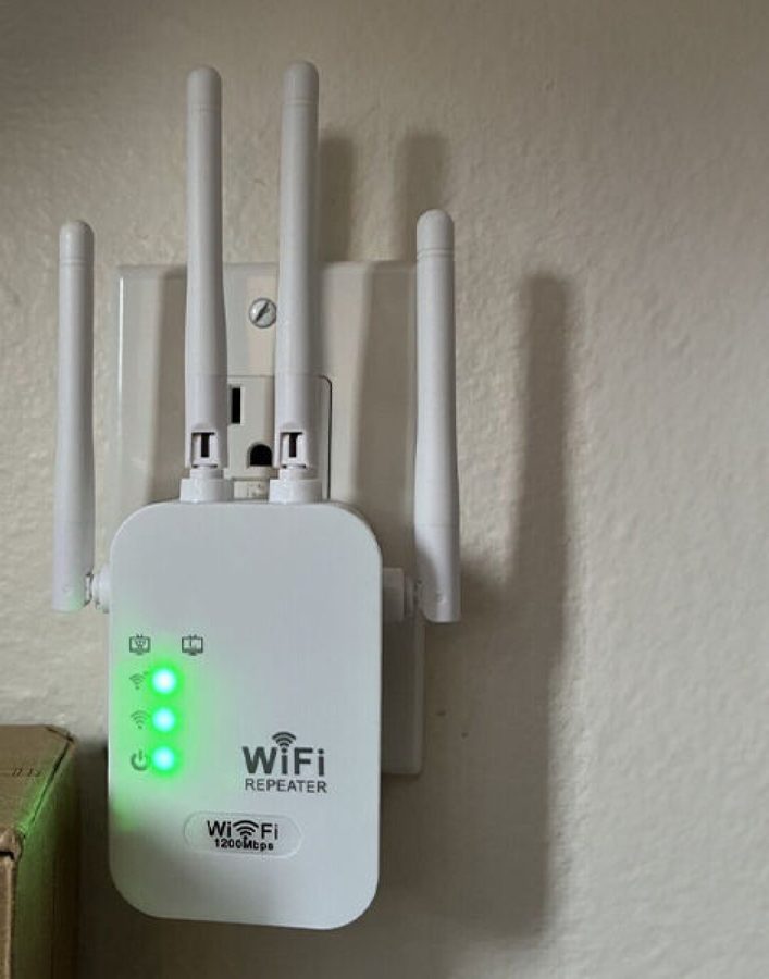 WiFi Boost Pro range extender plugged into a wall outlet with its four antennas up and green lights on
