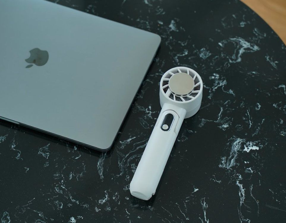 The WunderCool IceForce handheld fan standing on a desk beside a laptop