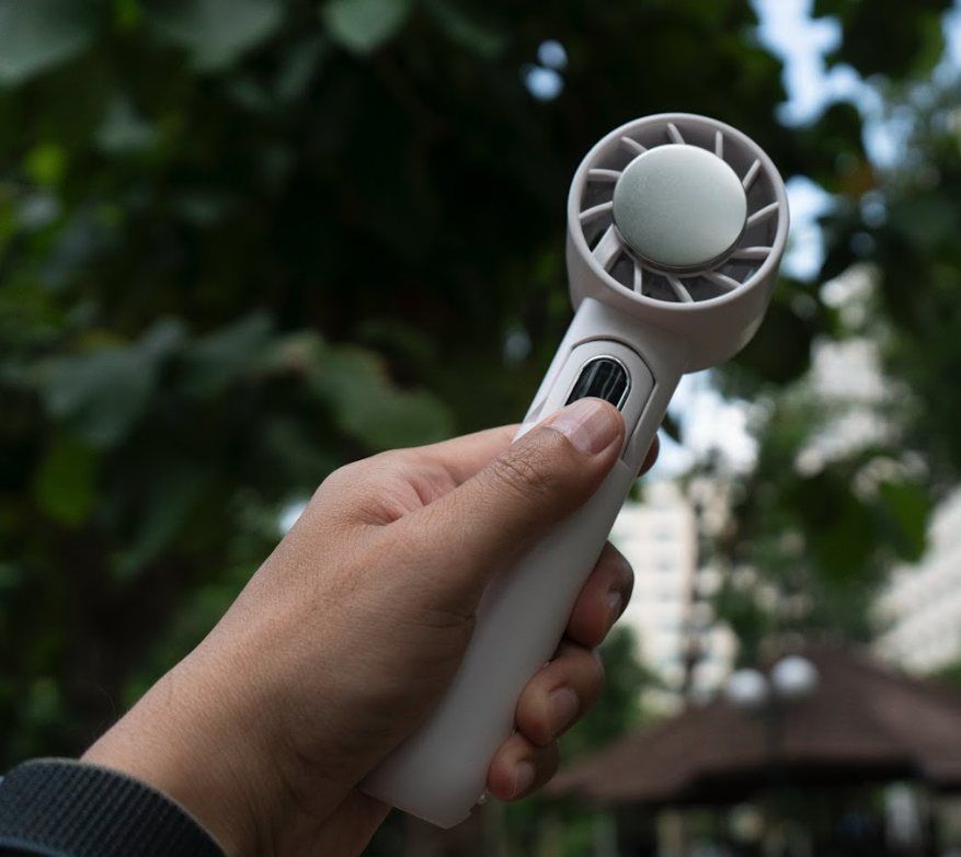 Hand holding the white WunderCool IceForce handheld fan outdoors