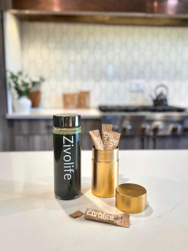 ZivoLife green drink bottle beside a gold tin of ZivoLife stick packs on a bright kitchen counter