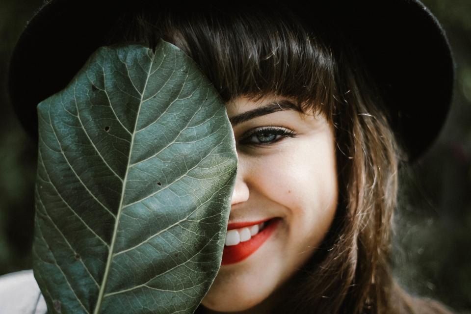Smiling woman in a black hat half hidden behind a large green leaf